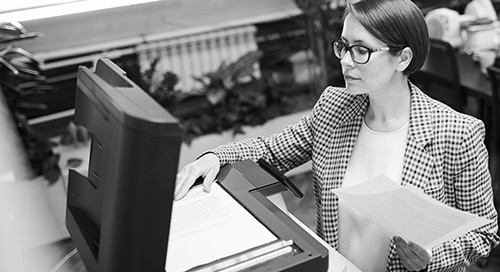 En affärskvinna står vid en stor kopieringsmaskin och skannar dokument.